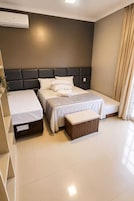 Una habitación de hotel con cama, mesita de noche, un pequeño banco y aire acondicionado instalado en la pared.