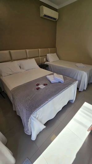 A hotel room with two beds, a headboard, an air conditioning unit, and a bedside table with a lamp. - Pousada Villa di Luri (Penha)