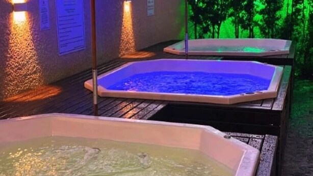 Two hot tubs with water, surrounded by walls with text and a wooden deck. - Pousada Villa di Luri (Penha)