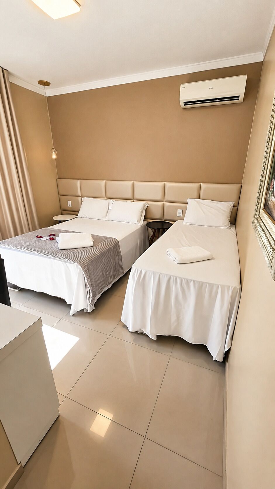 Habitación de hotel con dos camas, una mesita de noche, un equipo de aire acondicionado y un cuadro en la pared.