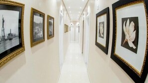 A hallway with framed pictures on the walls, a white floor, and doors at the end. - Pousada Villa di Luri (Penha)