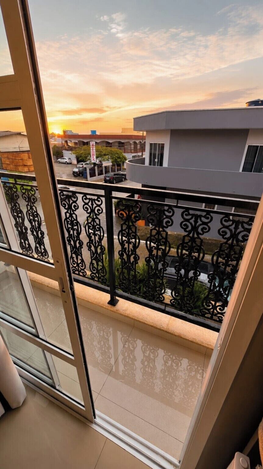 Ein Balkon mit Blick auf einen Sonnenuntergang, ein modernes Gebäude und eine Straße mit geparkten Autos.