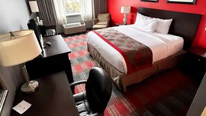 Quarto de hotel com cama, escrivaninha, cadeira e janela com cortinas.