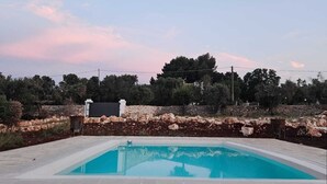 A rectangular swimming pool with a tiled deck, surrounded by a stone wall and vegetation. - Borgo Badessa Ostuni with a private pool (Puglia)