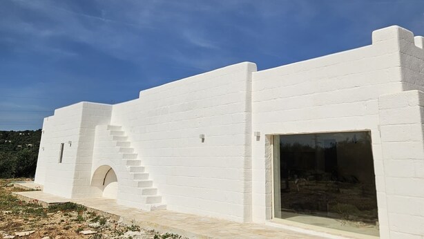 A white building with a staircase leading to an entrance, a large window, and a clear blue sky. - Borgo Badessa Ostuni with a private pool (Puglia)