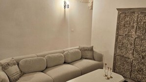 A living room with a sofa, a coffee table, a chair, a wall-mounted light, and a decorative cabinet. - Borgo Badessa Ostuni with a private pool (Puglia)