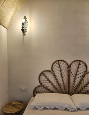 A bedroom with a bed, a wall-mounted light fixture, and a small wooden stool. - Borgo Badessa Ostuni with a private pool (Puglia)