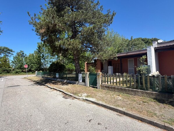 A residential street with a stop sign, a house with a fenced yard, and a large tree.