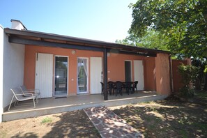 A building with a covered patio, a door, and a small outdoor seating area with chairs.