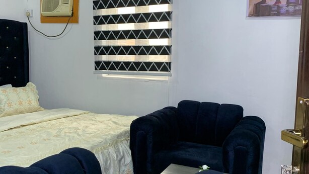 Ein Zimmer mit einem Bett, einem Schlafsofa, einem kleinen Tisch, einem Fenster mit Jalousien, einer Klimaanlage und einem Bild an der Wand.