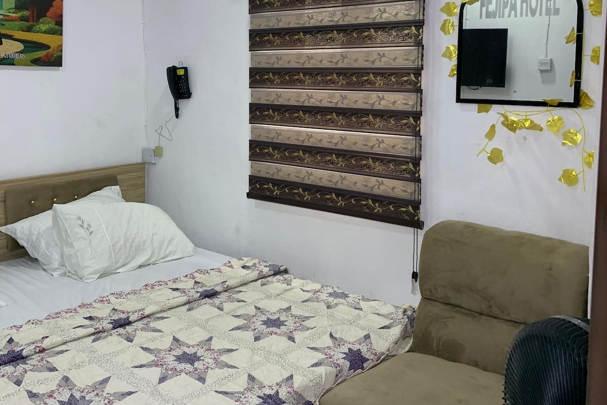 A hotel room with a bed, a sofa, a small table, a wall-mounted phone, a decorative mirror, and a painting.