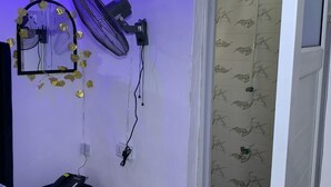 Quarto com cama, ventilador, espelho e porta para banheiro com azulejos estampados.