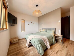 A bedroom with a bed, a television, a mirror, a bedside table with candles, and a woven light fixture. - Family Home, a 10-minute walk from the beach - 4 suites with private bathrooms (Quiberon)