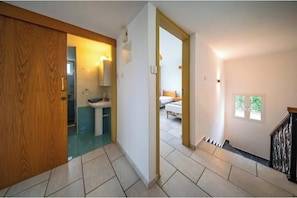 Ein Flur mit einer Holztür, ein Badezimmer mit Waschbecken und Toilette sowie ein Schlafzimmer mit Bett und Fenster.