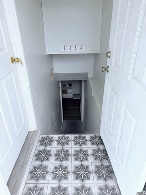 A hallway with a patterned floor, a door with a keyhole, and a small cabinet with a power outlet. - Entire Private Basement Suite – Not Just a Room (Layton)