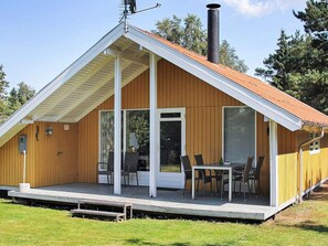 A wooden cabin with a pitched roof, a chimney, and a covered patio with chairs and a table. - 6 Person Holiday Home in Farvang (Farvang)