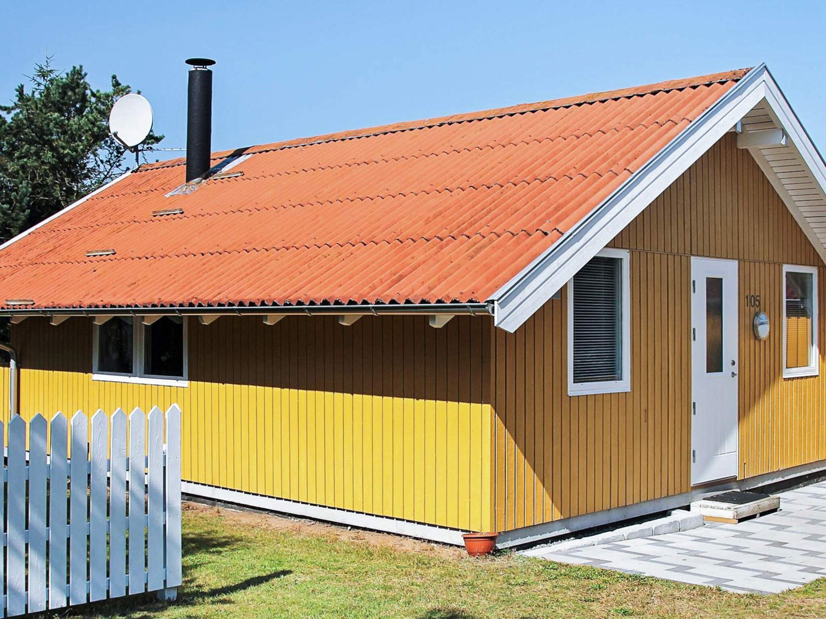 A single-story wooden building with a red roof, a white picket fence, and a small porch.