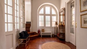 Una habitació àmplia amb terra de fusta, un tocador rodó de fibra natural, una banca, una cadira i una finestra gran d'arc.