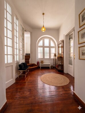 A spacious room with a wooden floor, a round woven rug, a bench, a chair, and a large arched window. - Unique! in the HEART of Athens Entire Building Apartment (Athina)