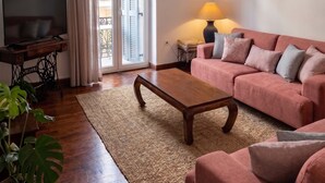 Un saló amb un sofà, una taula baixa, un televisor sobre un moble, una làmpada i una finestra amb cortines.