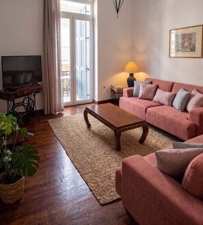 A living room with a sofa, a coffee table, a TV on a stand, a lamp, and a window with curtains. - Unique! in the HEART of Athens Entire Building Apartment (Athina)
