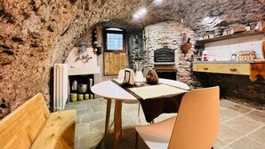 Un interior rústico de piedra con chimenea de piedra, una mesa de madera y un banco.