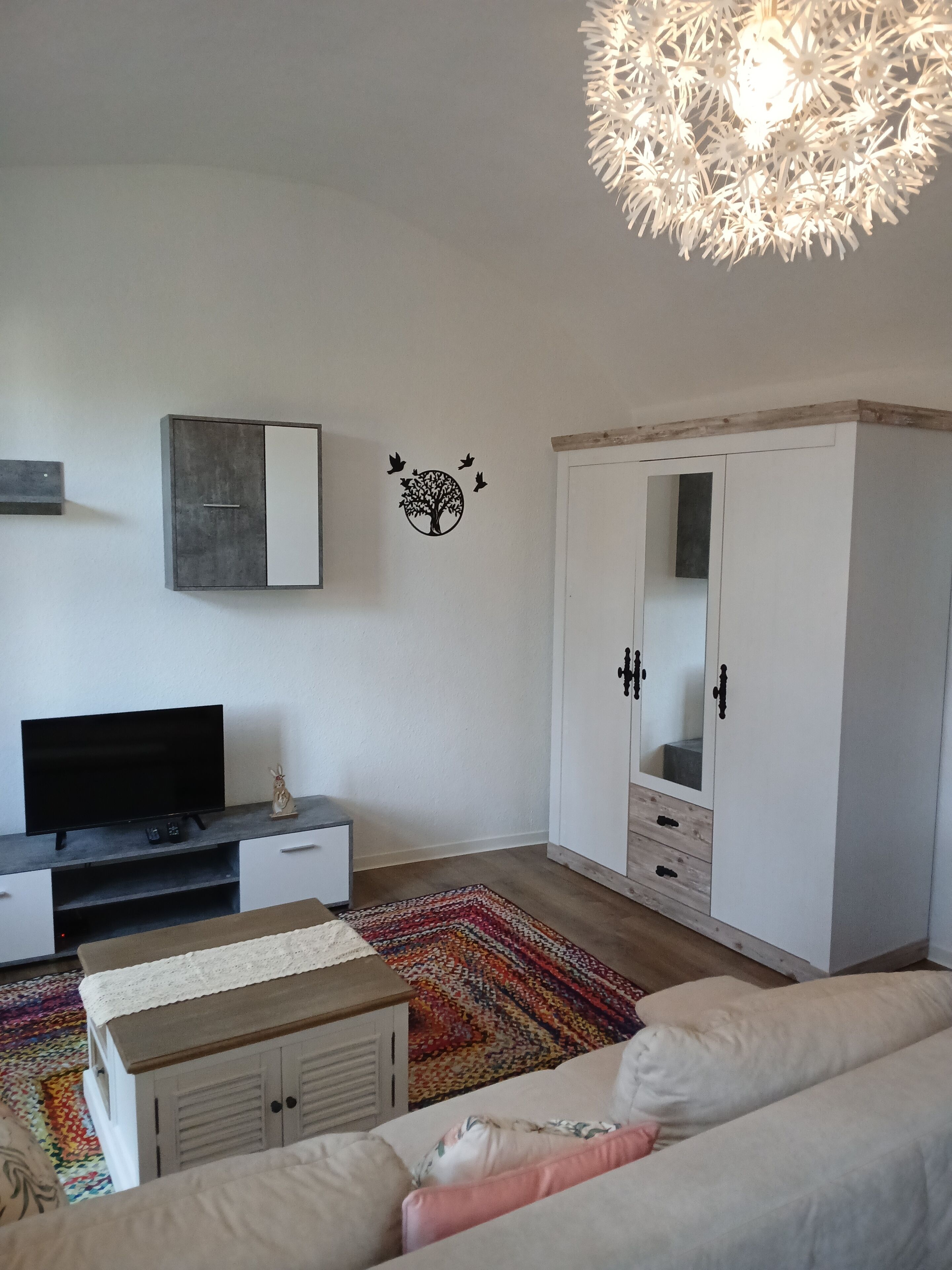 A living room with a television, sofa, wardrobe, and a decorative tree wall decal.