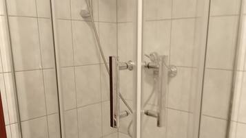 A glass-enclosed shower stall with white tiles, a handheld showerhead, and a wall-mounted faucet.