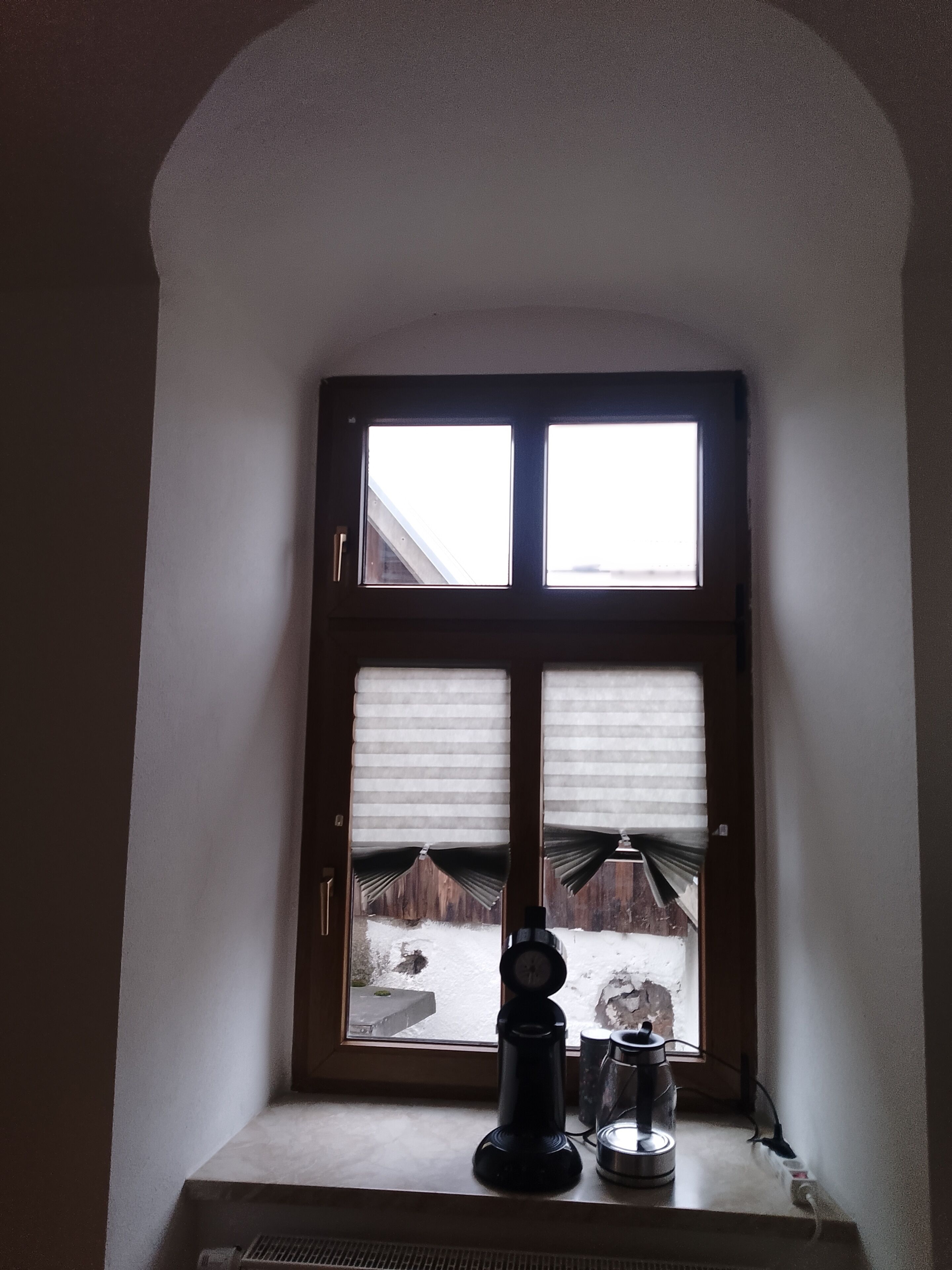 Et vindue med persienner, en kaffemaskine og en elkedel på et vindueskar.