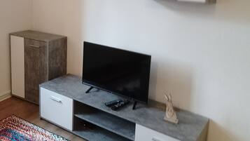 A modern living room with a flat-screen TV, grey cabinets, a small shelf, and a colorful rug.