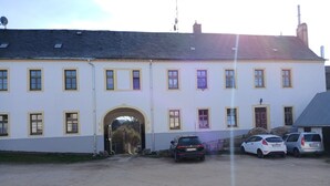 Un edificio con un arco central de entrada, varias ventanas y coches aparcados delante.
