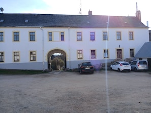 Un edificio con un arco central de entrada, varias ventanas y coches aparcados delante.