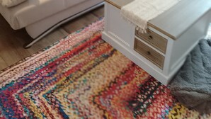 Una sala de estar moderna con un sofá, cojines, una mesita auxiliar blanca y una alfombra colorida.