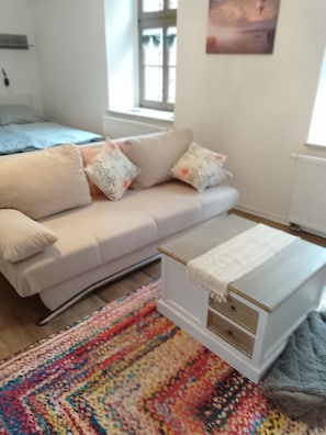 Una sala de estar moderna con un sofá, cojines, una mesita auxiliar blanca y una alfombra colorida.