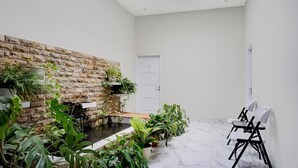 Une pièce avec un mur en pierre, une petite fontaine et plusieurs plantes en pot.
