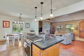 A spacious kitchen with a large island, a dining area with white chairs, and a cozy living room with a fireplace.