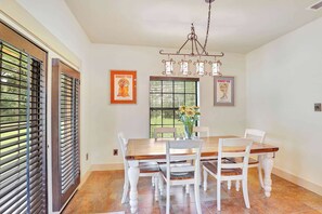 A dining area with a wooden table and white chairs, a chandelier, and two framed posters on the wall.