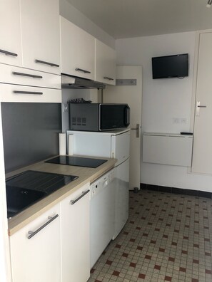 Una cucina compatta con mobili bianchi, un forno a microonde, un piano cottura e un frigorifero.