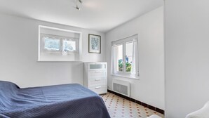 Et soveværelse med en seng, et kommode, en radiator og to vinduer.