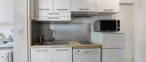 Una cocina compacta con armarios blancos, microondas, refrigerador y lavavajillas.
