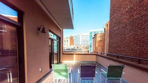 Ein Balkon mit zwei Stühlen, einer Glastür und Blick auf Gebäude.