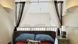 Ein Schlafzimmer mit Bett, Nachttisch, Lampe und einem Fenster mit Vorhängen.