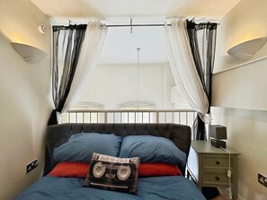 Ein Schlafzimmer mit Bett, Nachttisch, Lampe und einem Fenster mit Vorhängen.