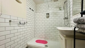 Ein Badezimmer mit weißen Fliesen, einer Dusche, einem Waschbecken und einem Handtuchhalter.