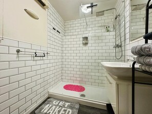 Ein Badezimmer mit weißen Fliesen, einer Dusche, einem Waschbecken und einem Handtuchhalter.