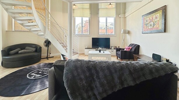 Ein modernes Wohnzimmer mit Treppe, Flachbildfernseher und großem Fenster.