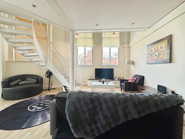 Ein modernes Wohnzimmer mit Treppe, Flachbildfernseher und großem Fenster.