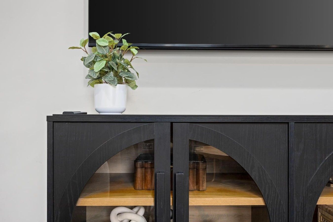A black cabinet with a glass door, a white vase with a plant, and a flat-screen TV mounted above.