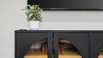 A black cabinet with a glass door, a white vase with a plant, and a flat-screen TV mounted above.