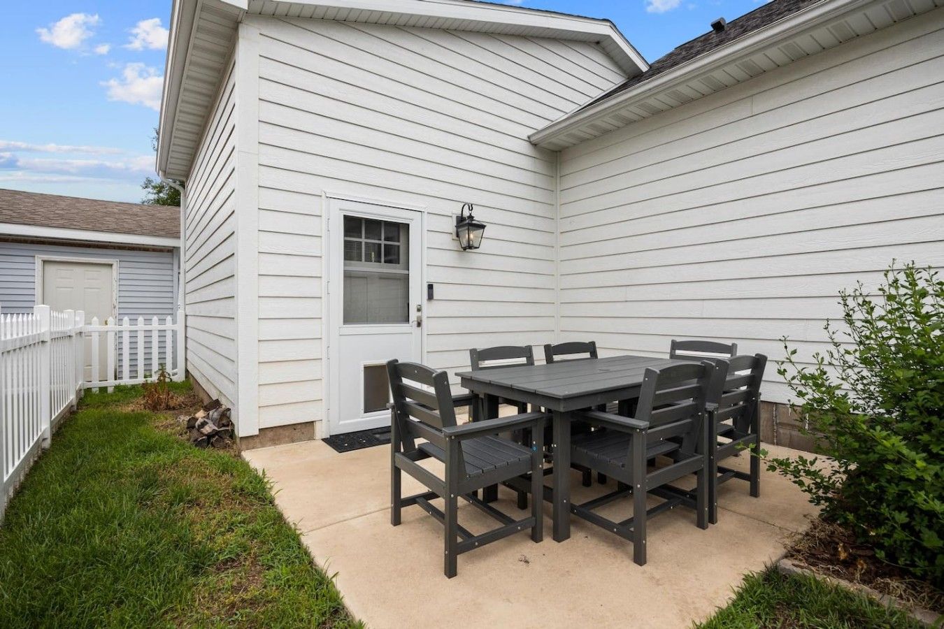 Une terrasse avec une table et des chaises, une clôture blanche et une maison recouverte de bardage.
